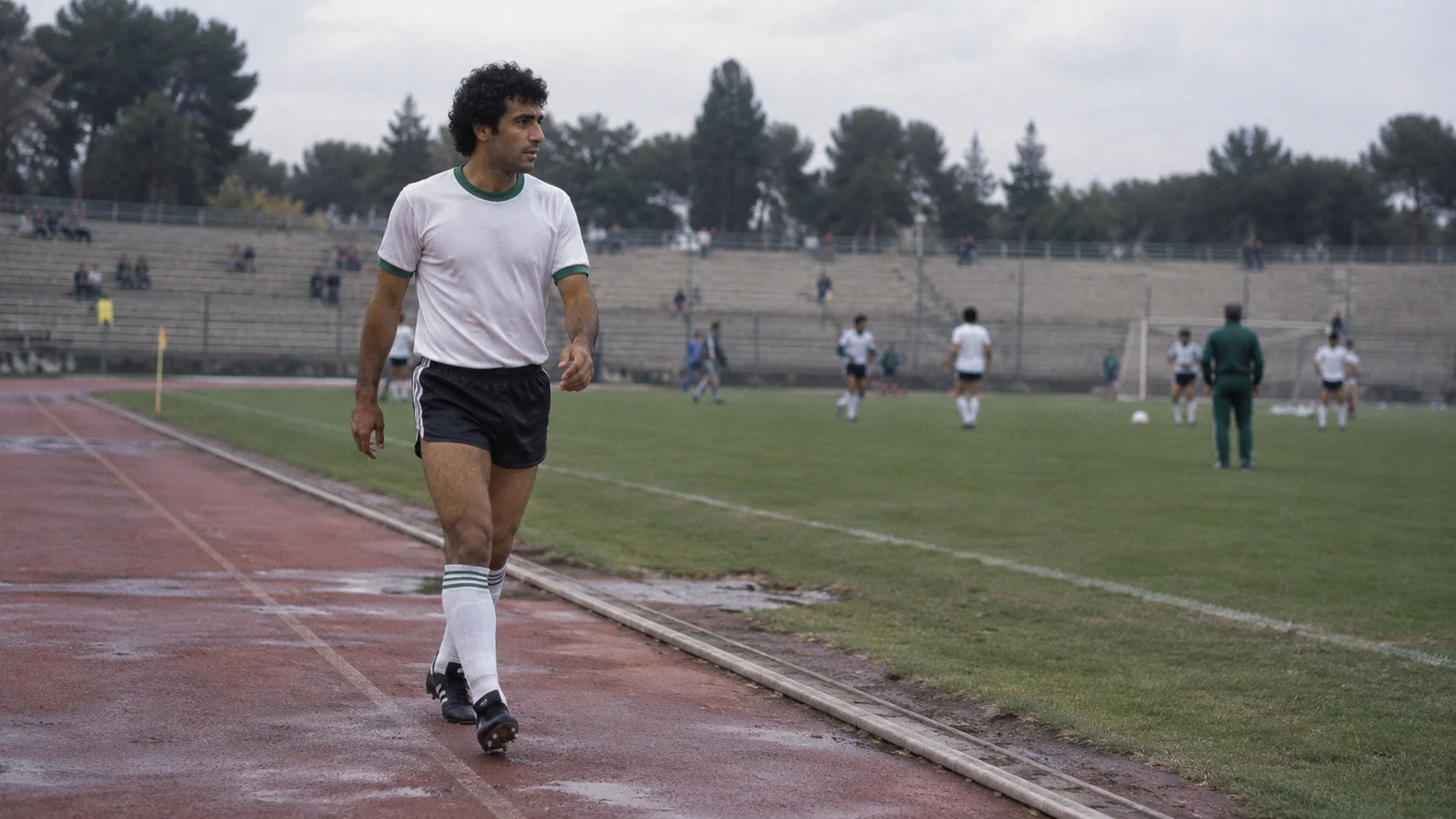 لاعب بملابس كرة قدم بسيطة يمشي بجوار مضمار ملعب قديم